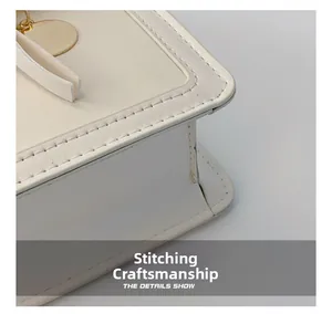 Macro shot of fine stitching craft and golden circular pendant on cream crossbody bag