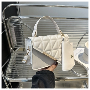 Close-up of white quilted handbag with golden metal trim and matching mini pouch
