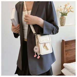 Detail of mini cream crossbody bag with adjustable strap and pink plush doll charm