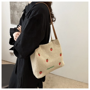 Dettaglio borsa in paglia intrecciata con ricami di fragole rosse e manici in pelle