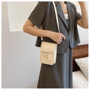 Detail of minimalist beige phone crossbody bag with gold text and elegant leather tassel