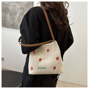 Dettaglio borsa a tracolla in paglia con ricamo di fragole e cinturino in pelle marrone