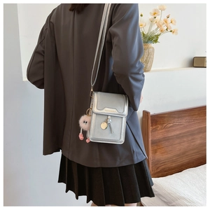 Rear view of model wearing a mini silver crossbody phone bag with a pink pompom charm