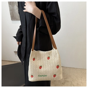 Detail of straw woven bucket bag with strawberry embroidery and leather strap