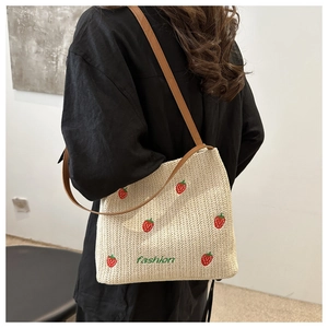 Dettaglio borsa di paglia intrecciata a mano con ricamo di fragole e tracolla in pelle