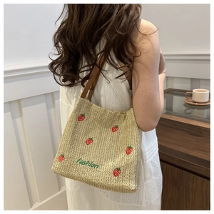 Straw tote bag with strawberry embroidery and leather handles shown on a model
