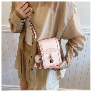 Detail view of pink mini crossbody phone bag with cute pompom charm on a female model