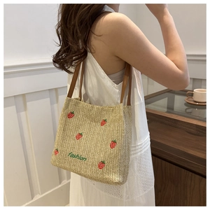 Dettaglio della borsa in paglia beige con ricamo a fragola e spalline in pelle marrone