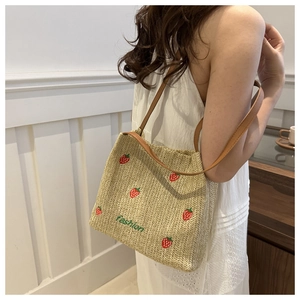 Dettaglio borsa di paglia con ricamo a fragola e scritta fashion con manici in pelle