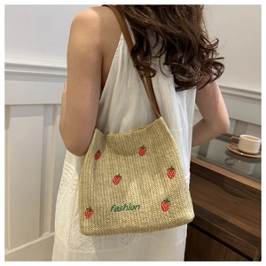 Detailed view of woven straw shoulder bag featuring embroidered strawberries and leather strap