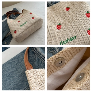 Close-up of straw woven tote with red strawberry embroidery and brown leather straps