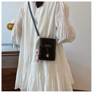 Close-up of black PU leather mini crossbody bag with gold hardware and plush monster charm