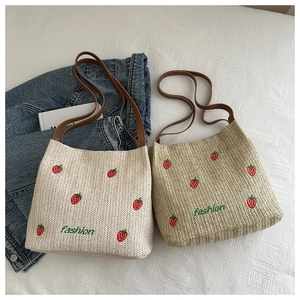Dettaglio della borsa in paglia con ricamo di fragola rossa e scritta fashion verde