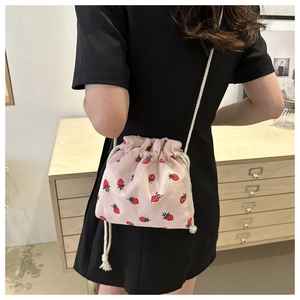 Detail of strawberry print corduroy drawstring bucket bag worn by a model in a cozy room