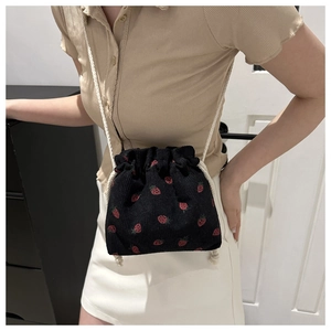 Gros plan d'un sac seau en velours noir à motif fraise avec bandoulière en corde