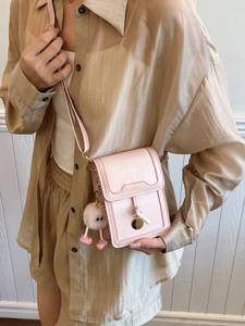 Mini pink crossbody phone bag with cute monster charm on a model's neutral outfit
