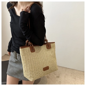 Detail of hand-woven straw tote with brown PU leather trim and knotted shoulder strap