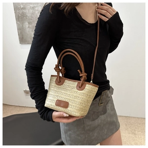 Detalle del bolso tipo cubo de paja con asas de cuero marrón y etiqueta de marca