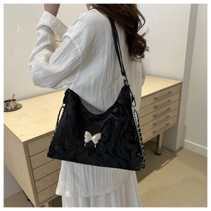Chic black glossy shoulder bag with silver butterfly charm and chain strap on a model