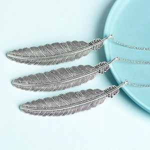 Vintage silver feather pendants with fine carved textures on light blue background