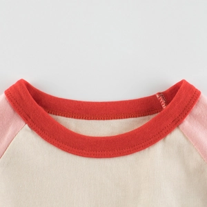 Primo piano della t-shirt raglan per bambini con girocollo rosso e cuciture rosa manica