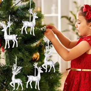 Close-up of a child hanging clear acrylic reindeer ornaments on a warm lit Christmas tree