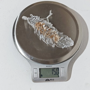 Weight display of a transparent acrylic feather ornament with gold sequins showing 15.0g