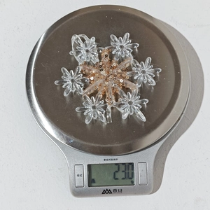 Detail shot of a clear acrylic snowflake ornament with gold sequins on a digital scale