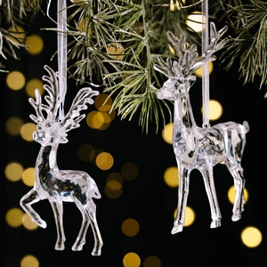 Clear acrylic Christmas reindeer pendants hanging on green pine branches with bokeh lights