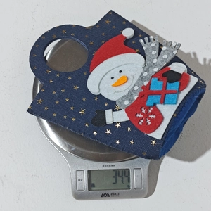 Detailed view of snowman felt Christmas gift bag on scale showing light weight of 34g