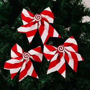 Three red and white striped Christmas bows with candy centers on green tree branches