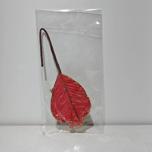 Detail of red Christmas leaf ornament with gold glitter edges in clear packaging