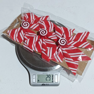 Three red and white striped Christmas bows weighing 29.1 grams on a digital scale