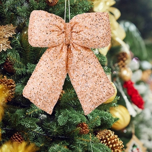 Macro detail of champagne sequin Christmas bow pendant hanging on a festive tree
