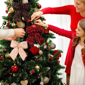 Close-up of sparkling sequin bows being hung on a Christmas tree during family decoration