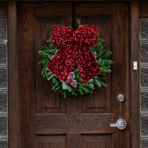 Detail of green Christmas wreath with large red sequin bow on a wooden door