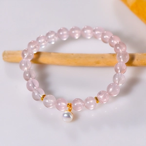Pink quartz 8mm beaded bracelet with white pearl charm and gold spacers on wooden stand