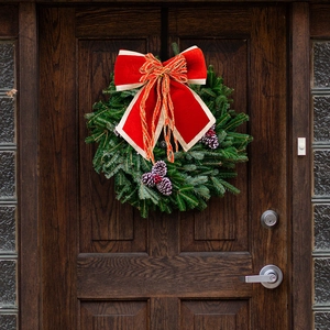 Close-up of a Christmas wreath with a large red velvet bow and golden edges on a wooden door