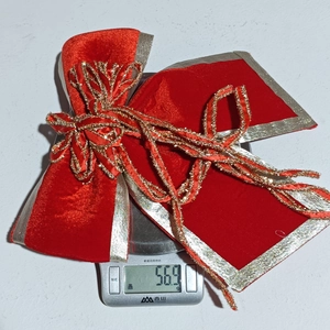 Detail of red velvet Christmas bow with gold glitter edges on an electronic scale weighing 56.9g