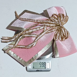 Detail shot of a luxury pink velvet Christmas bow with gold trim weighing 59.8g on a scale