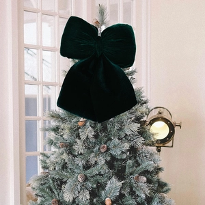 Detail of a large dark green velvet bow ornament placed on a snowy Christmas tree topper