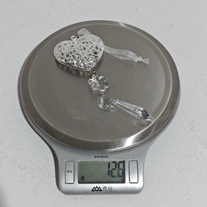 Gros plan d'un pendentif en acrylique argenté en forme de cœur pesant 12,6 g sur une balance