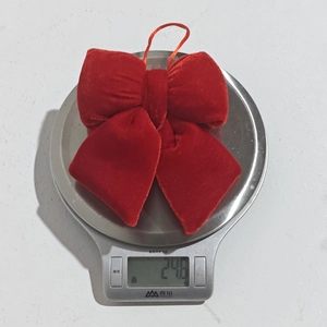 Red velvet Christmas bow ornament shown on an electronic scale weighing 24.0 grams