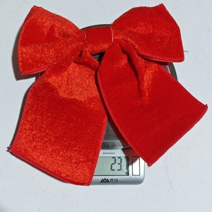 Vue macro du nœud de Noël en velours rouge sur balance affichant un poids léger de 23,1g