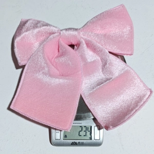 Pink velvet Christmas bow weighing 23.4 grams on a scale showing its lightweight quality