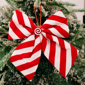Detail of red and white striped Christmas bow ornament hanging on a snowy Xmas tree branch