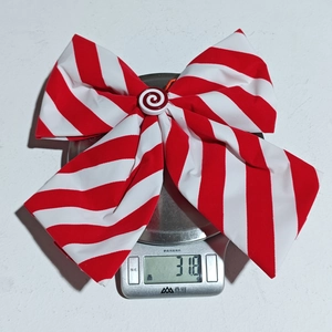 Detail view of red and white striped Christmas bow ornament weighing 31.8g on a digital scale