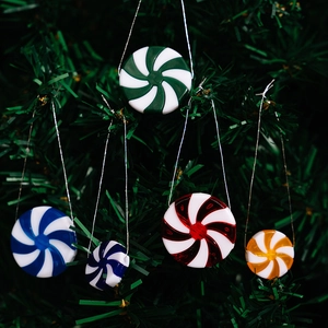 Close-up of colorful peppermint candy ornaments hanging on a green Christmas tree branch