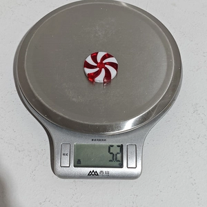 Macro shot of a red and white spiral candy ornament weighing 5.2g on a digital scale