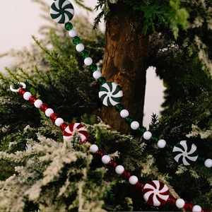 Detail of peppermint candy bead garland hanging on snowy pine branches for Christmas decor